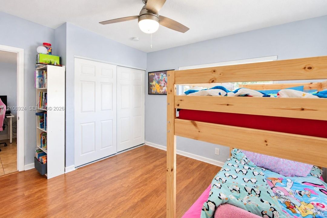 Room featuring wood-finish flooring, a ceiling fan with light fixture, and dual-panel sliding closet doors