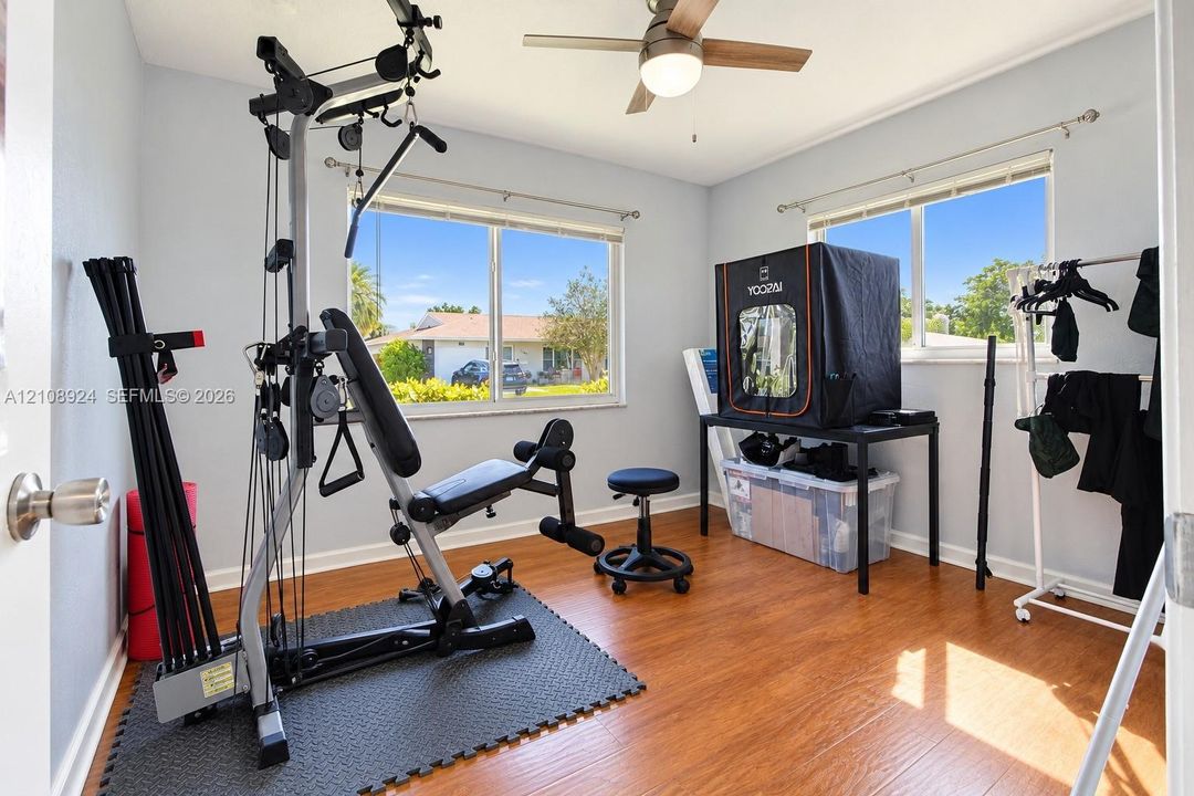 Room featuring wood-finish flooring, dual windows, and a ceiling-mounted light fixture with a fan