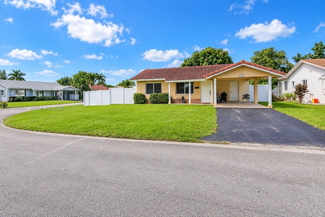 Single-story residence featuring a tile roof, covered carport, paved driveway, and white vinyl privacy fencing
