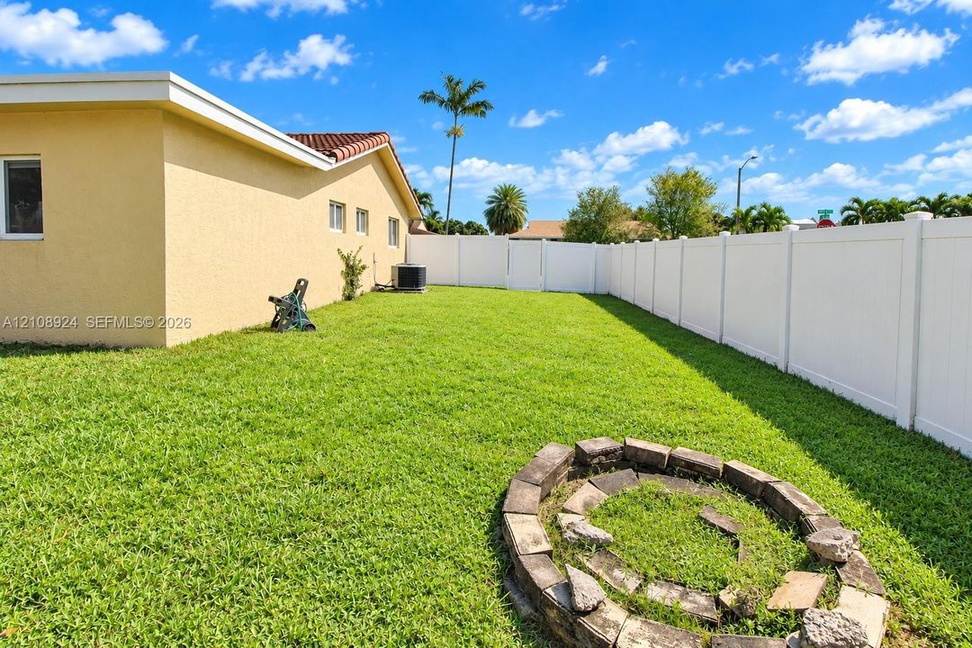 Stucco exterior residence featuring a level backyard, white vinyl privacy fencing, and a circular stone-block fire pit