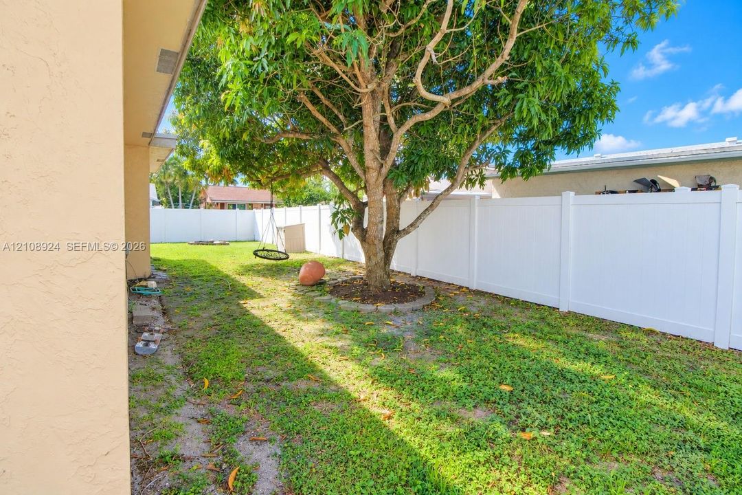 Fenced backyard featuring a manicured lawn, established shade tree, and a stone-bordered garden bed