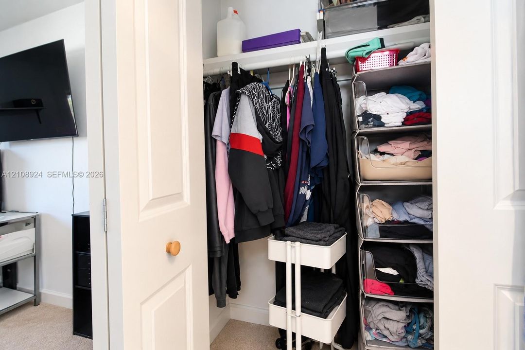 Reach-in closet featuring dual-panel doors, a single integrated hanging rod, and an elevated storage shelf