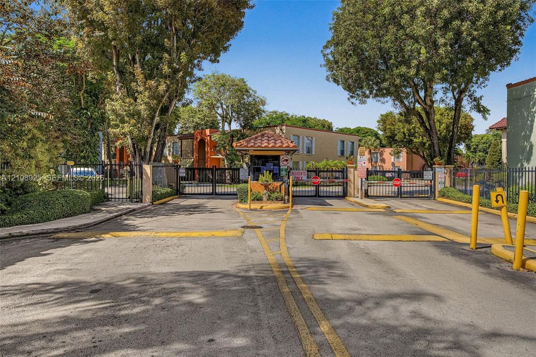 Gated entry point featuring a secured vehicular access gate, a covered guard station with a terracotta tile roof, and perimeter metal fencing