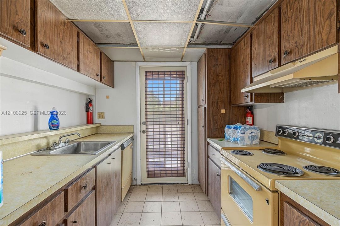 Kitchen featuring wood-finish cabinetry, tile flooring, stainless steel sink, and a built-in range