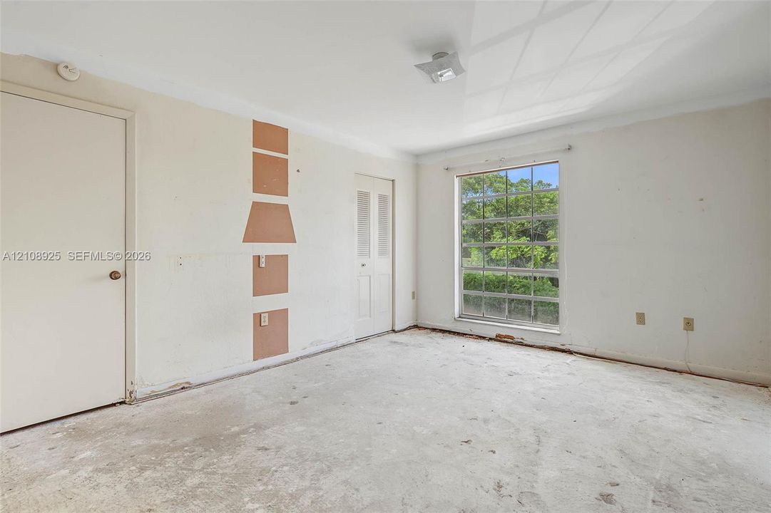 Interior space featuring a large window with multi-pane grid detailing, neutral-toned walls, a louvered closet door, a solid-panel door, and a central ceiling-mounted light fixture