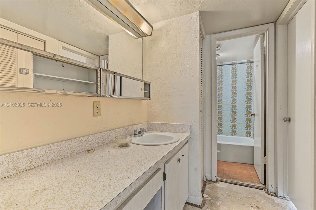 Bathroom featuring a vanity with a laminate countertop, integrated oval basin, chrome-finish faucet, and built-in mirrored medicine cabinet with integrated lighting