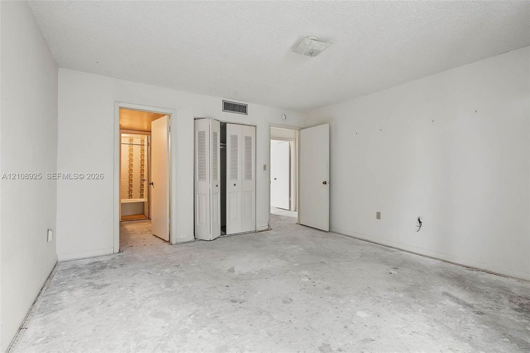 Room featuring dual reach-in closets with louvered doors, a walk-in closet, and a flush-mount ceiling light fixture