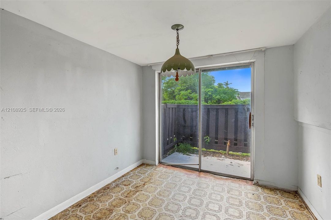 Sliding glass door opening to a private concrete patio with a perimeter wood fence, featuring geometric pattern flooring and a dome-style pendant light fixture