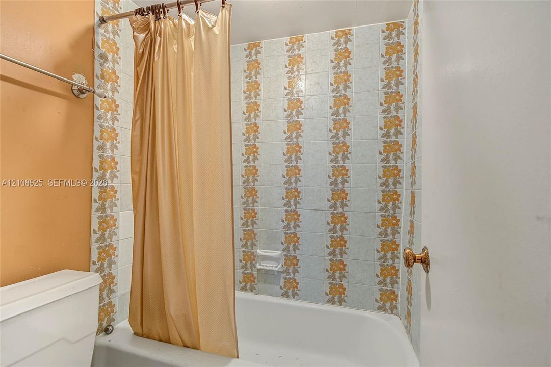 Bathtub and shower combination featuring floral-patterned ceramic tile surround, recessed soap dish, and wall-mounted metal curtain rod