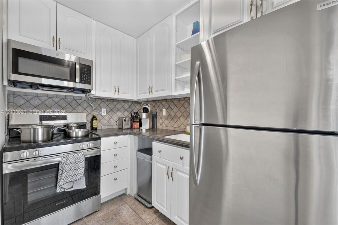 Kitchen featuring white cabinetry, stainless steel appliances, dark stone-finish countertops, ceramic tile backsplash, and tile flooring