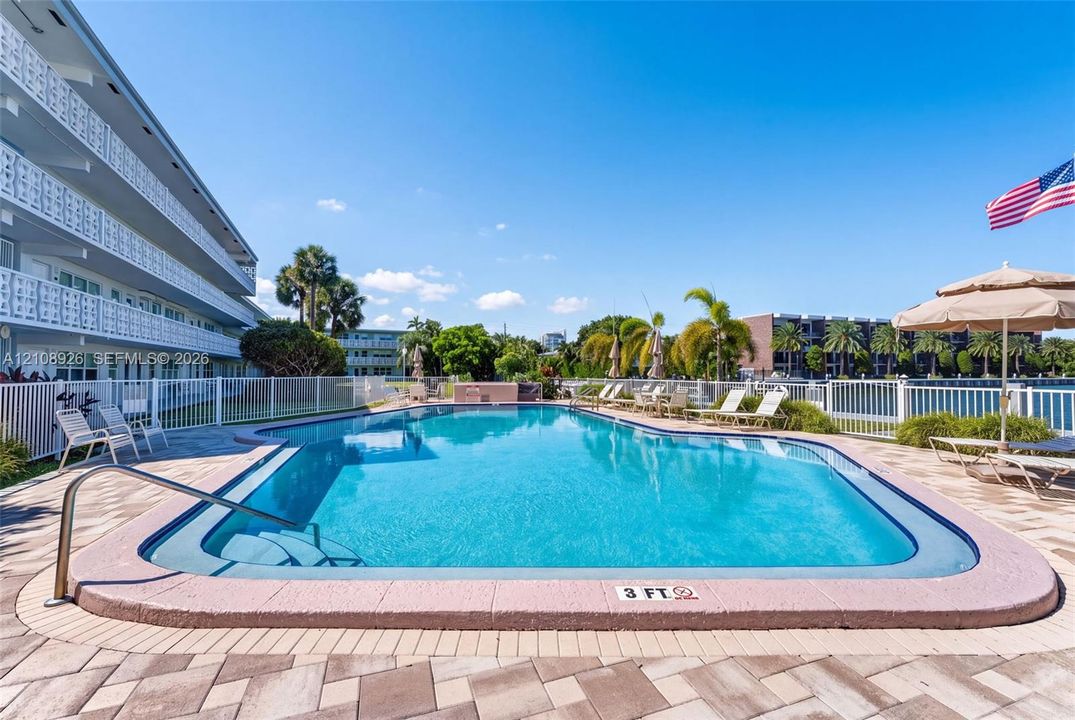 In-ground swimming pool featuring a brick paver deck, metal safety fencing, and palm tree landscaping