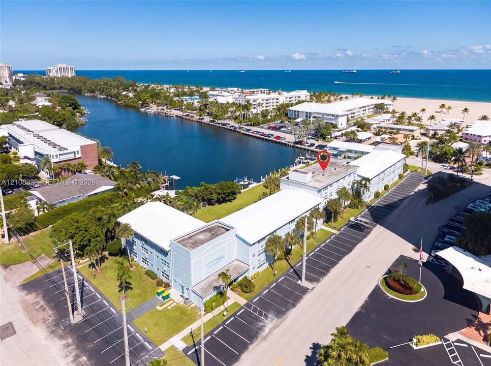 Multi-story residential building featuring exterior parking, landscaped green space, and coastal positioning