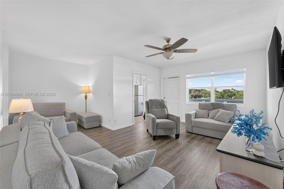 Living area featuring wood-finish flooring, a ceiling fan with integrated lighting, and a large window