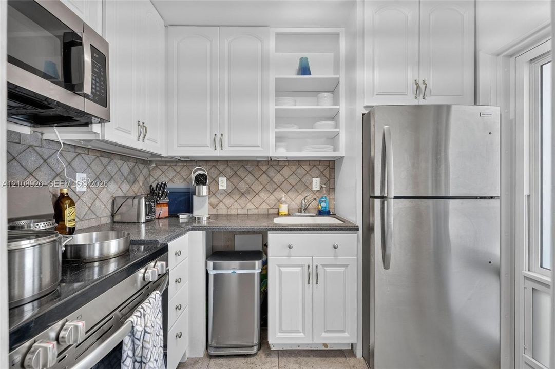 Kitchen featuring white cabinetry, stainless steel appliances, dark stone-finish countertops, open shelving, and a tiled backsplash
