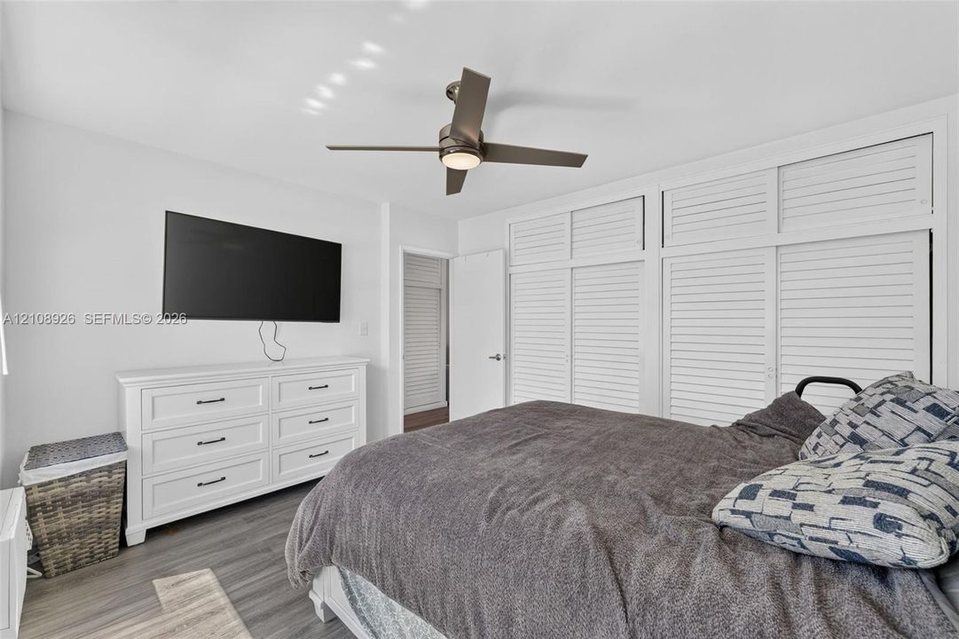 Bedroom featuring wood-finish flooring, floor-to-ceiling built-in white louvered-style cabinetry, and a central ceiling fan with integrated lighting