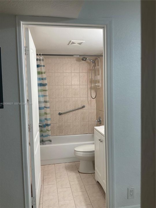 Bathroom featuring a shower-tub combination with ceramic tile surround, integrated metal grab bar, white vanity cabinet, and tile flooring