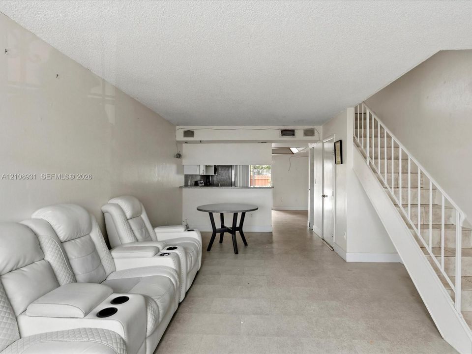 Open-concept interior featuring neutral-toned tile flooring, a staircase with a white railing, and a pass-through counter opening to a kitchen area