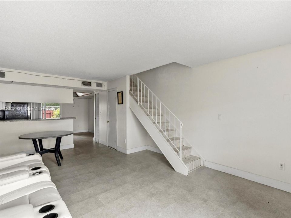 Open-concept interior featuring tile flooring, a built-in kitchen breakfast bar, and a staircase with a metal handrail