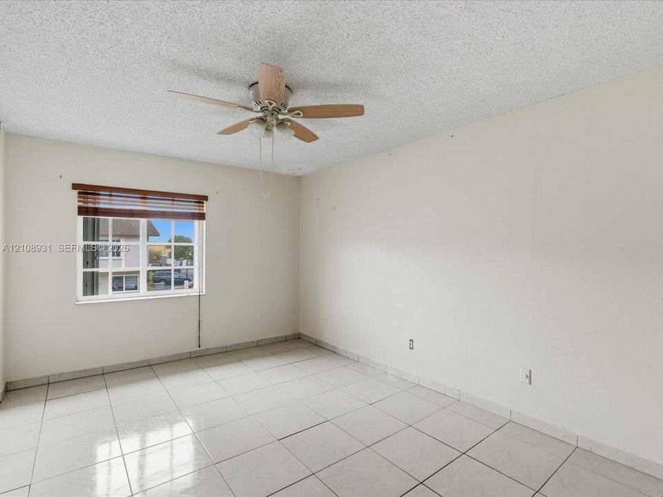Interior space featuring large-format ceramic tile flooring, a multi-blade ceiling fan with integrated lighting, and a dual-pane window with a horizontal blind