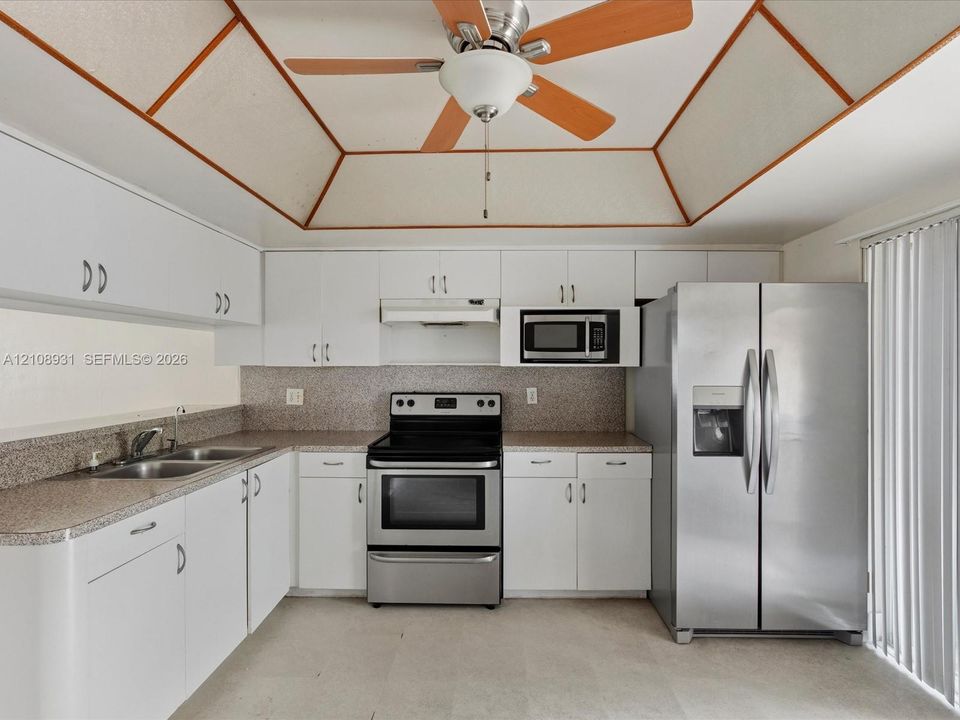 Kitchen featuring white cabinetry, speckled stone-finish countertops, stainless steel appliances, and a tray ceiling with wood trim accents