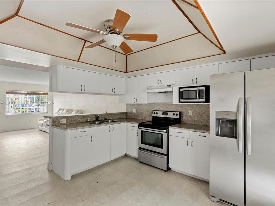 Kitchen featuring a tray ceiling with wood trim, white cabinetry, speckled stone-finish countertops, stainless steel appliances, and a ceiling fan