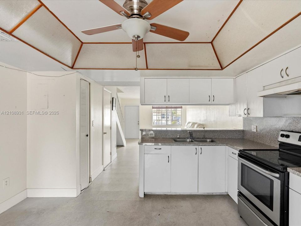 Kitchen featuring white cabinetry, stone-finish countertops, stainless steel electric range, tray ceiling with wood trim, and ceiling fan with integrated lighting