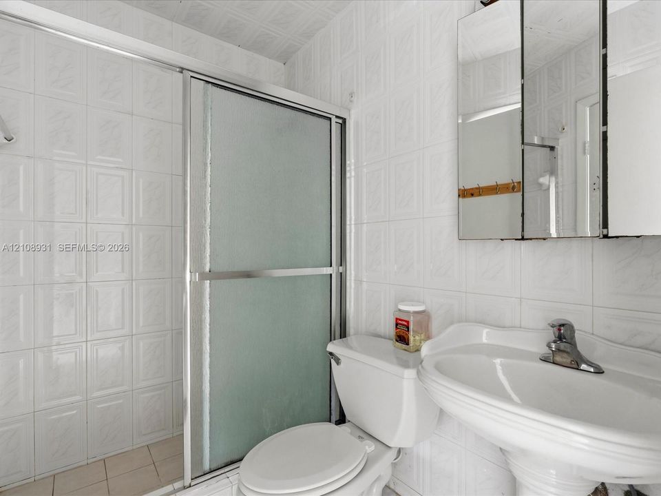 Full-wall ceramic tile surround, pedestal sink with chrome faucet, shower enclosure with sliding glass doors, and mirrored medicine cabinet