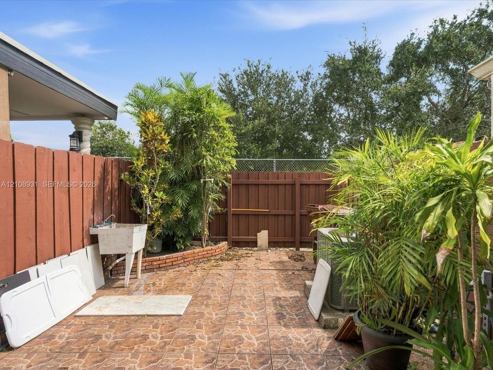 Private patio featuring stone-pattern tile flooring, a perimeter wood privacy fence, and a built-in utility basin