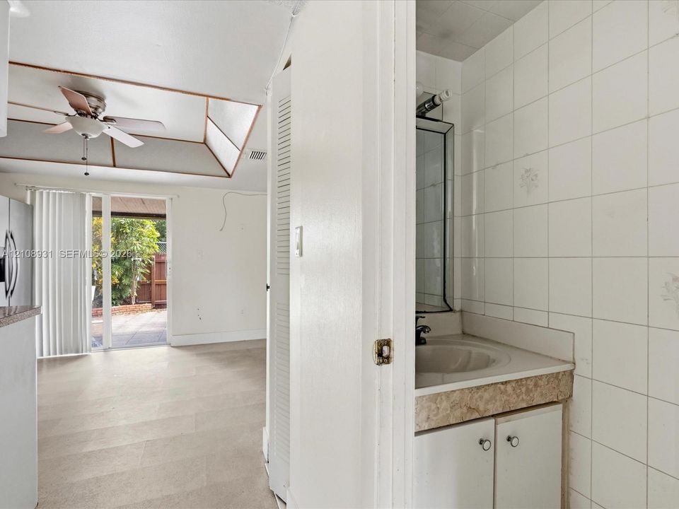 Bathroom featuring a single-sink vanity with stone-finish countertop and full-height tiled walls, set within a space showcasing a tray ceiling and sliding glass door access to the exterior