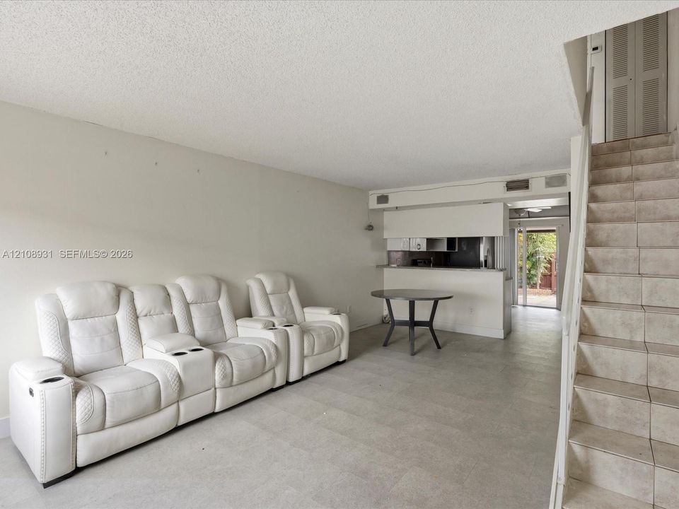 Open-concept interior featuring large-format tile flooring, a kitchen pass-through counter, and a staircase with tiled treads