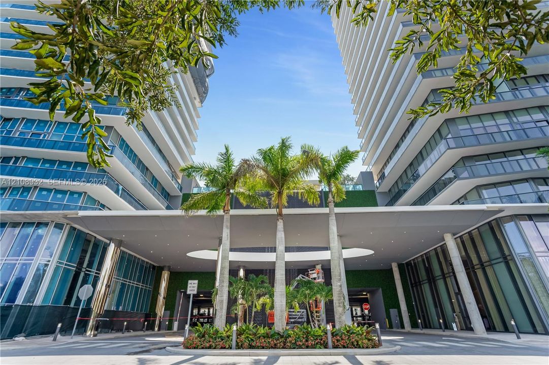 Contemporary high-rise architecture featuring glass facade paneling, covered porte-cochère, recessed lighting, and integrated landscaping with mature palm trees