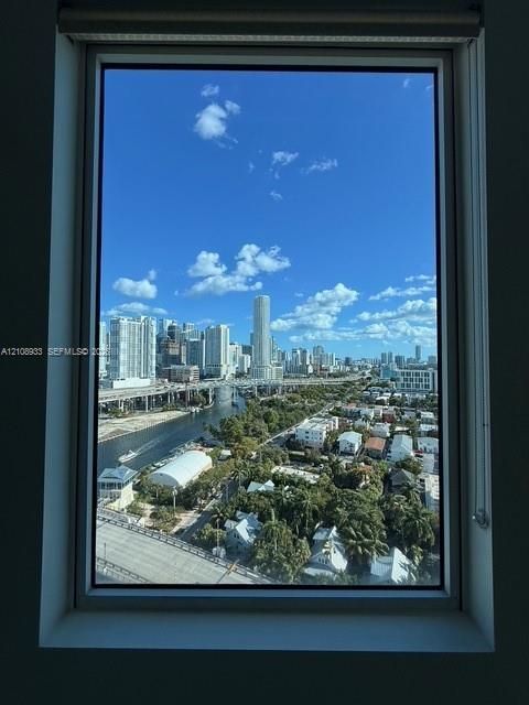 Floor-to-ceiling window framing a cityscape including urban skyscrapers, a waterway, and dense tree canopy