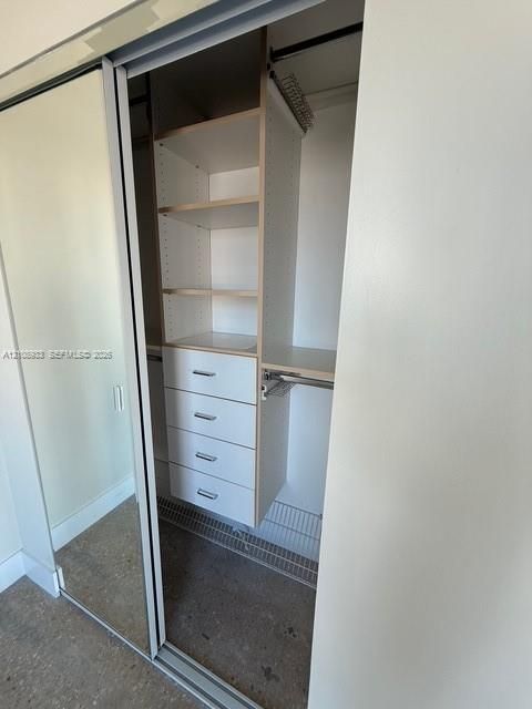 Closet featuring sliding mirrored doors, integrated white cabinetry with four pull-out drawers, multiple open storage shelves, and overhead clothing rods