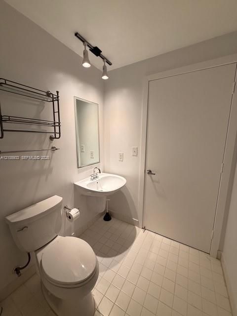 Wall-mounted pedestal sink with polished chrome dual-handle faucet, rectangular wall-mounted mirror, ceiling-mounted track lighting, and tiled flooring