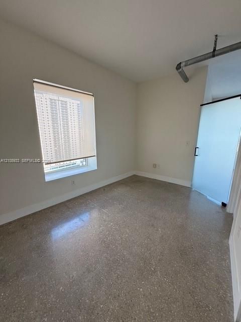 Interior space featuring polished concrete flooring, neutral wall tones, a large window with a fitted roller shade, and a frosted glass sliding door