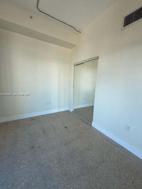 Interior room featuring speckled stone-finish flooring, neutral wall coloring, and a closet with sliding mirrored doors