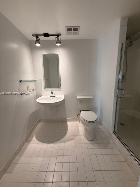 Wall-mounted pedestal sink with chrome faucet, tiled floor, glass-enclosed shower, rectangular mirror, and dual-bulb track lighting