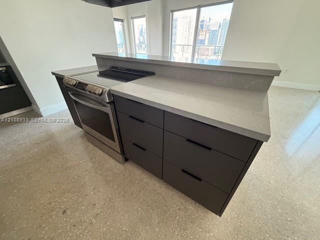 Kitchen island featuring a stone-composite countertop, matte grey flat-panel cabinetry with horizontal pulls, stainless steel slide-in range, and polished concrete flooring