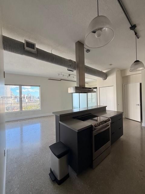 Industrial-style loft space featuring polished concrete flooring, exposed ductwork, a kitchen island with an integrated cooktop, a stainless steel range hood, and pendant lighting