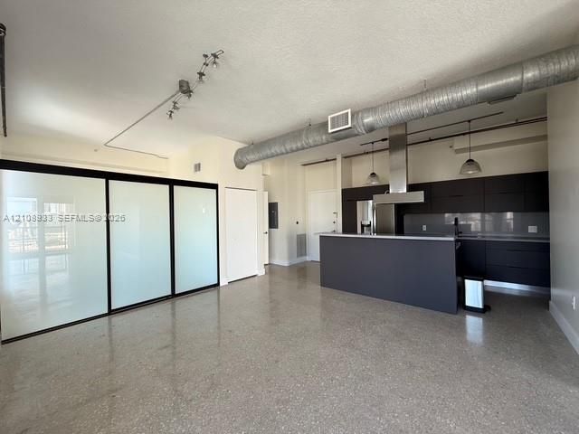 Open-concept interior featuring polished concrete flooring, industrial-style exposed ductwork, a kitchen with dark cabinetry and a stainless steel vent hood, and large sliding translucent glass privacy panels