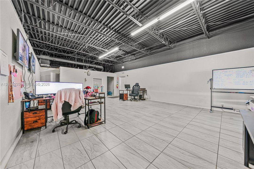 Open-concept interior featuring light-toned ceramic tile flooring, an industrial-style exposed ceiling, and linear fluorescent lighting