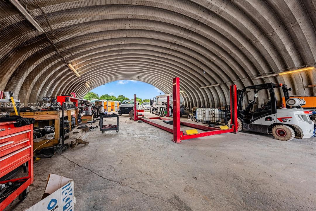 Quonset-style structure featuring a high-clearance arched metal roof, concrete flooring, and a built-in automotive lift system