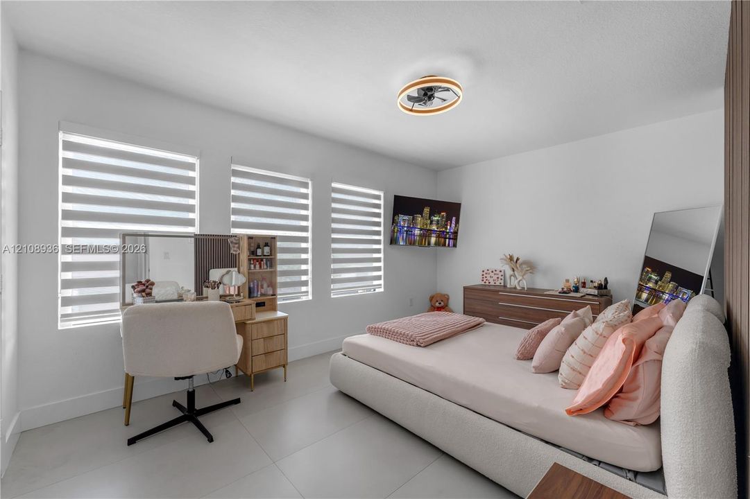 Neutral-toned ceramic tile flooring, three large windows with installed zebra shades, and a modern circular low-profile LED ceiling fixture