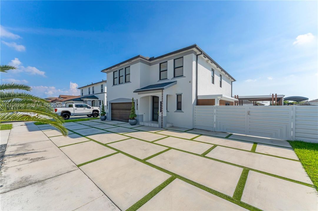 Stucco exterior featuring a wood-finish garage door, geometric concrete paver driveway with turf insets, and white horizontal privacy fencing