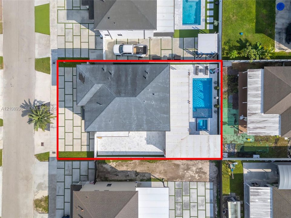 Aerial perspective of property featuring a private swimming pool with integrated spa, paver patio, and expansive paved driveway