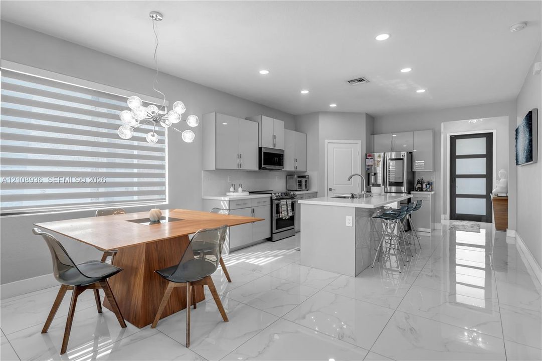 Kitchen featuring high-gloss cabinetry, a central island with a stone-finish countertop, stainless steel appliances, recessed lighting, and large-format porcelain tile flooring