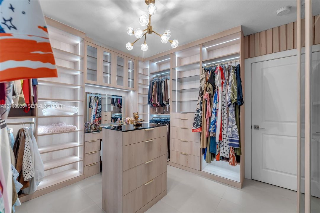 Custom closet featuring floor-to-ceiling cabinetry, integrated LED shelf lighting, a central storage island with a dark countertop, and an eight-light chandelier