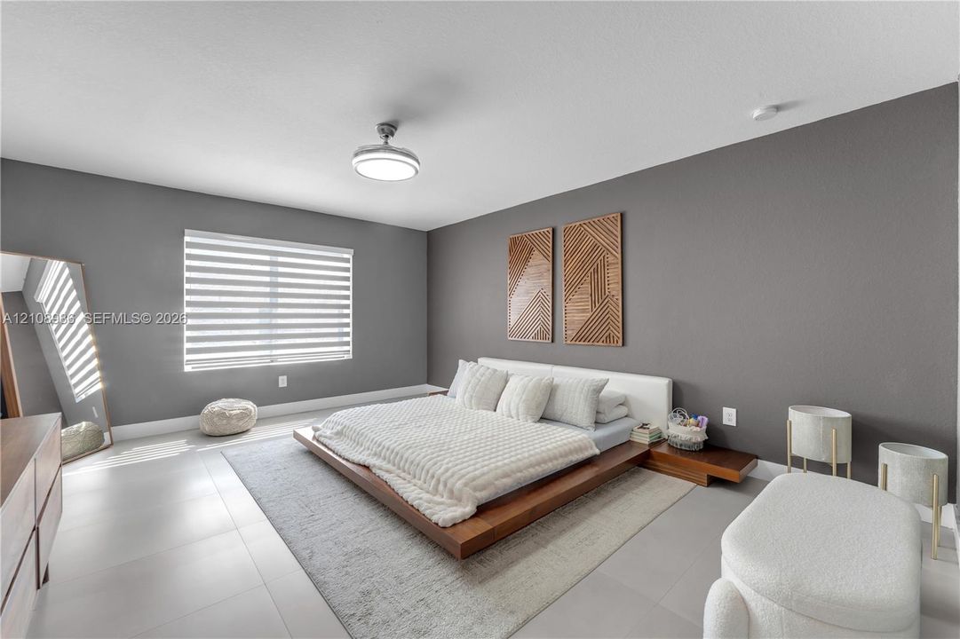 Room featuring neutral grey walls, large-format tile flooring, a horizontal window with dual-layer shades, and a circular flush-mount ceiling fan