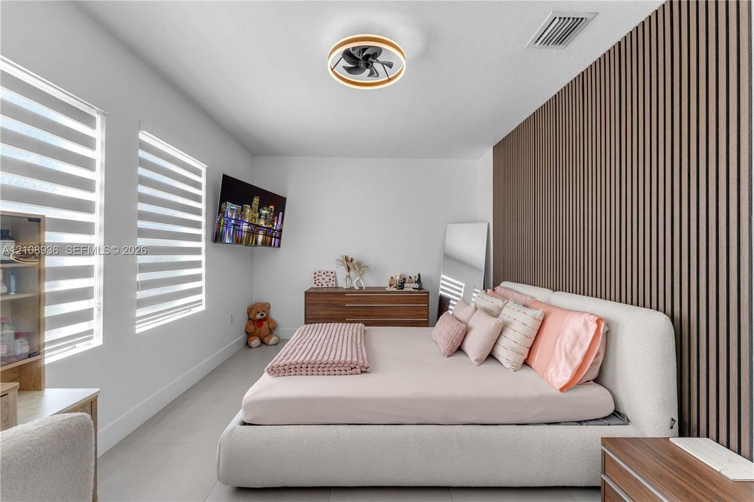 Room featuring a floor-to-ceiling wood-slat accent wall, tile flooring, dual-layered roller shades, and a modern circular ceiling fan with integrated lighting