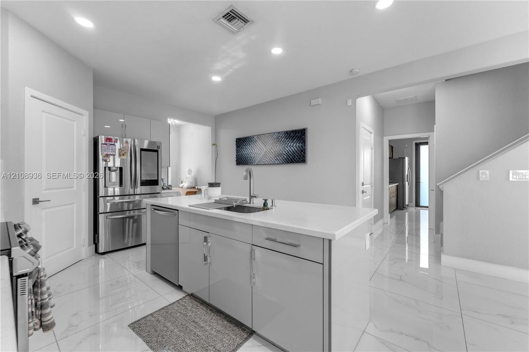 Kitchen featuring a central island with a solid surface countertop, high-gloss cabinetry, stainless steel appliances, and large-format tile flooring